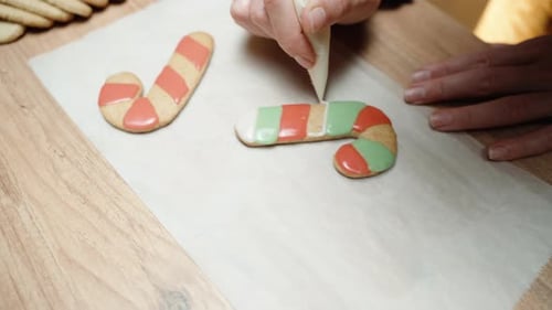 Preparing homemade Christmas gingerbread candy cane cookies, the woman is decorating them with strip