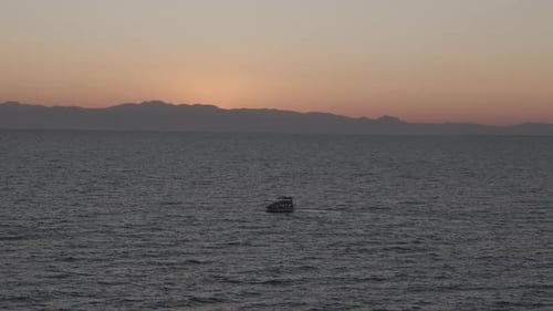 Small sailing boat travelling across Mediterranean sea towards glowing orange sunset skyline