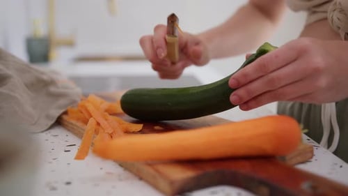 Woman approaching kitchen sink to peel cucumber. Close up, handheld
