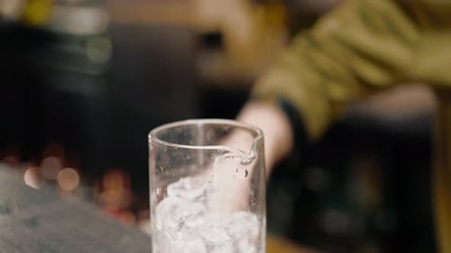 close-up of a bartender pours ice cubes into a cocktail glass in preparation of delicious cocktails