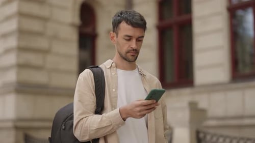 Man with Backpack Checks His Phone on City Street