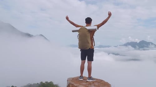 Asian Hiker Male Reaching Up Top Of Foggy Mountain Standing On The Rock And Raising His Hands