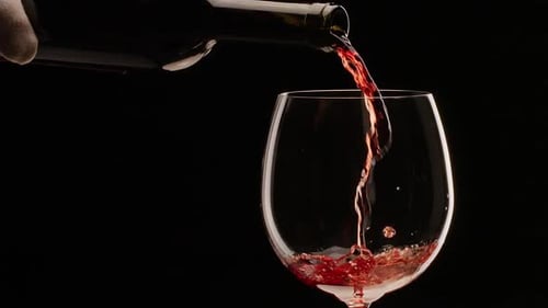 Red wine is pouring into a glass on a black background. Slow motion, close shot.