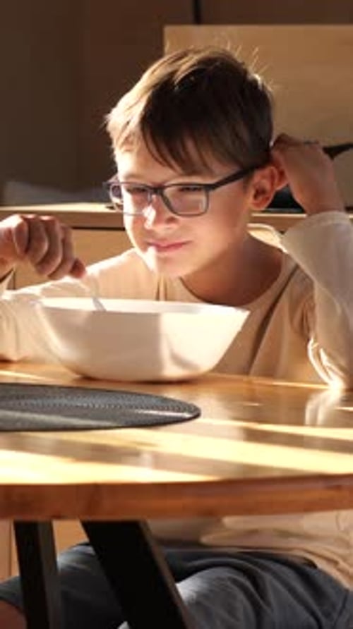 Vertical Video Young Boy with Glasses Enjoying Bowl of Cereal at Breakfast Time
