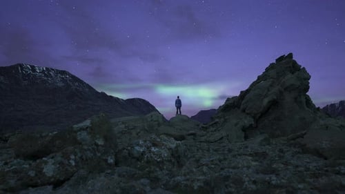 Caminhante aventureiro em um pico rochoso e acidentado. Céu dramático com estrelas e aurora boreal. Colorido