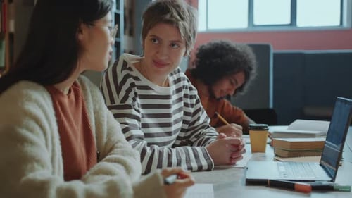 Two Female Students Discussing College Project on Laptop in Library
