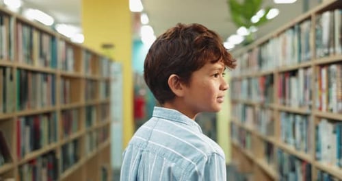 Happy boy, walking and library with bookshelf for knowledge, story or learning literature