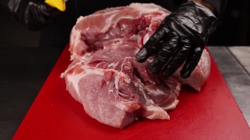 A butcher cuts a pig carcass on a red board