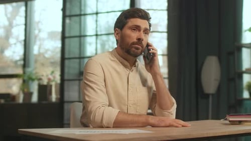 Serious Man Talking on Smartphone at Workplace Table