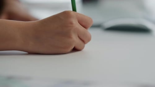 Child Hand Drawing with Green Pencil on Desk