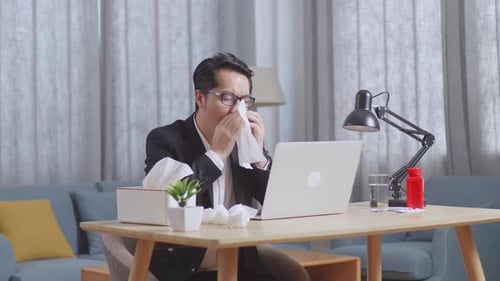 Sick Businessman While Working With Laptop At Home. Sick Guy Blows Sneezes Wipes Snot Into Tissue