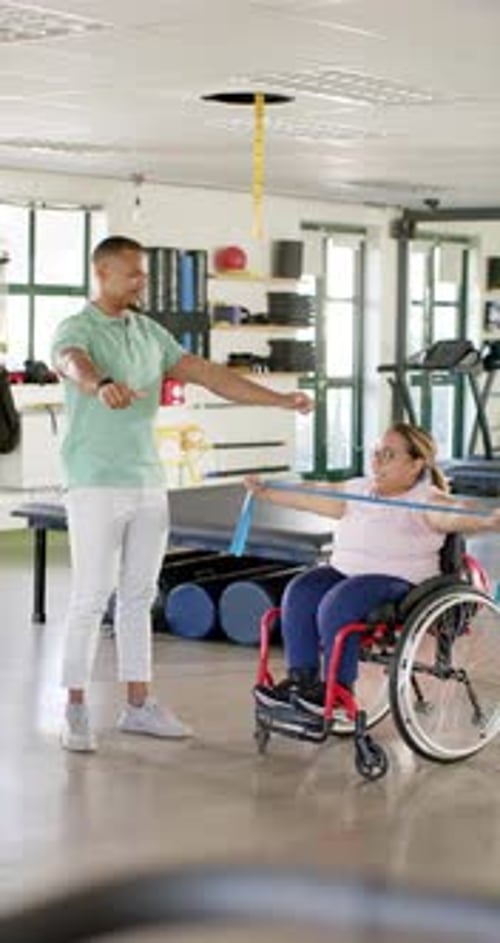 Vertical video: In rehabilitation center, exercising with resistance band, woman in wheelchair and t