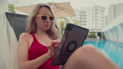 Woman Uses Tablet by Tropical Swimming Pool