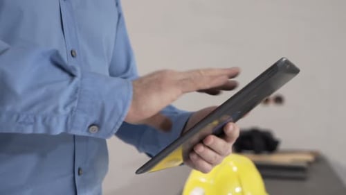Young man working with tablet and blueprints in his new apartment