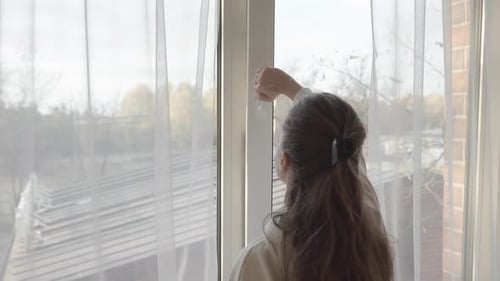 A woman closes a slightly ajar PVC plastic window and pulls the curtains.