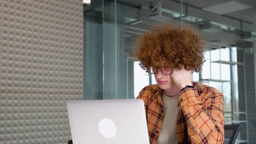 Young Freelancer or Blogger in Glasses with Braces Working on a Laptop in Office