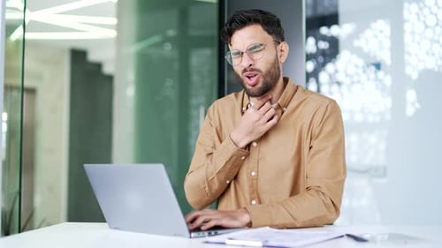 Man Coughing at Desk Holding His Throat