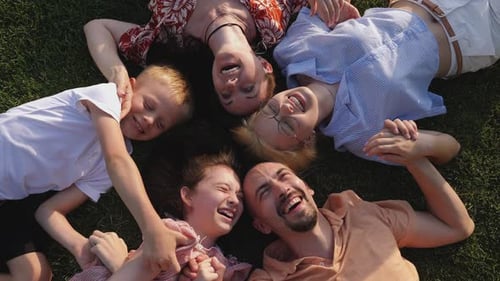 A Big Happy Family Lies on a Green Lawn in a Circle and Laughs Top View