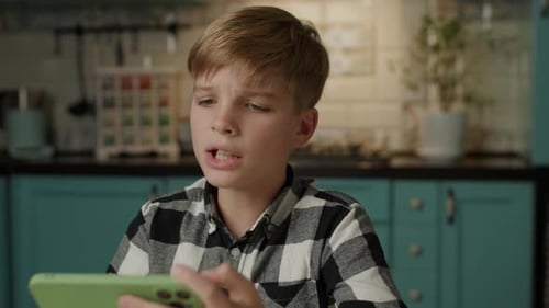 Blond Boy Focused on Smartphone in Kitchen