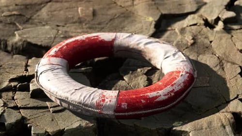 Weathered Red and White Lifebuoy on Coastal Rocks