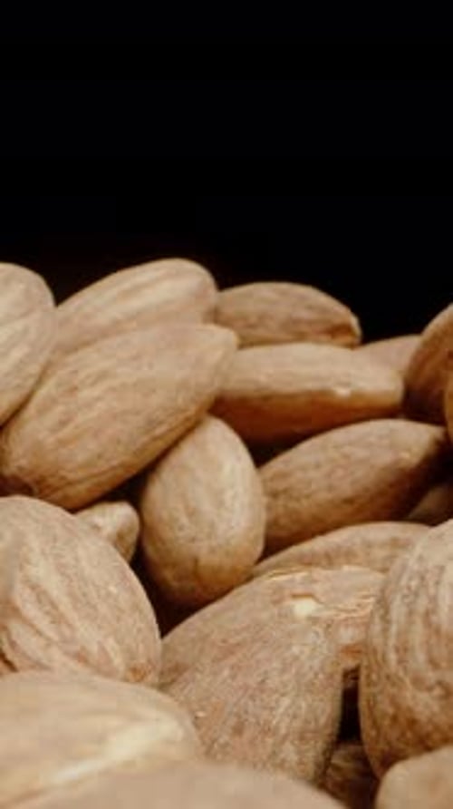 Vertical video. Close-Up of a Hand Taking a Handful of Almonds. Isolated on a Black Background.