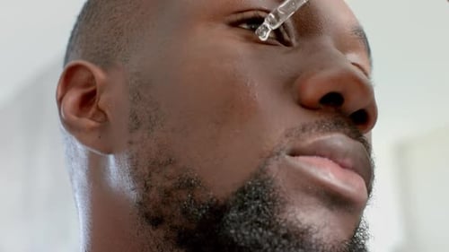 Applying serum on face, African American man enjoying skincare routine at home spa