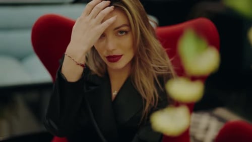 Elegant Woman Sitting in Red Chair with Confident Expression in Urban Setting