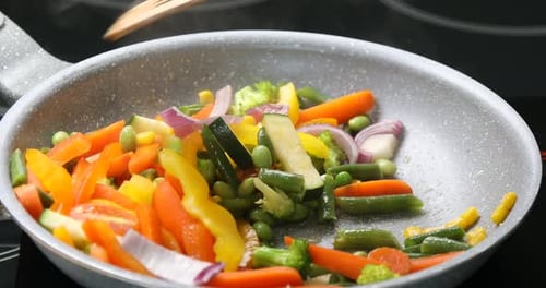 Verschiedene leckere Gemüsesorten in der Pfanne mit Spatel auf dem Herd kochen, Nahaufnahme