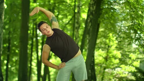 Young Man Stretching in a Lush Green Forest
