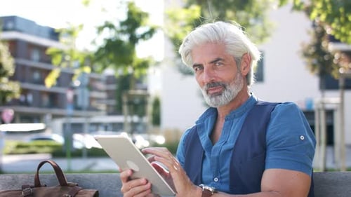 Portrait of Mature Man with Tablet Sitting Outdoors in City, Looking At