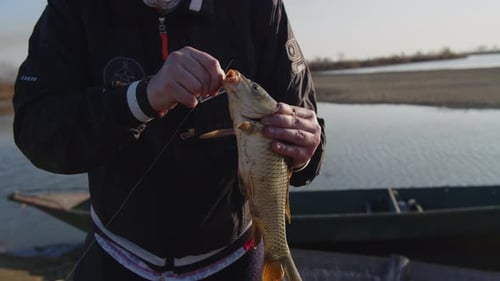 Fisherman Removes Hook from Fish by River