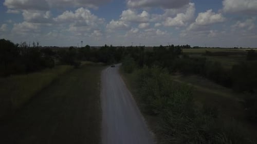 Aerial tracking shot of a red car traveling down a quiet road
