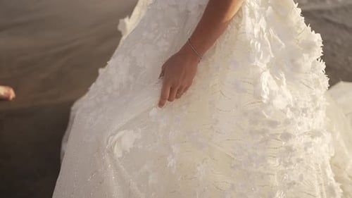 Close-up of a bride's hand gently holding her detailed lace wedding gown
