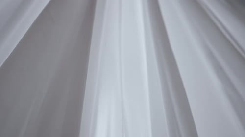 Transparente weiße Seidenstoffe, die aus einem offenen Fenster schweben und durch den Schatten weiches Licht scheinen