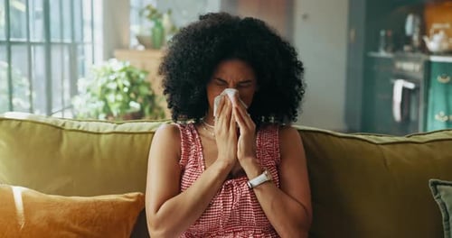 Woman, sneeze and tissue on sofa in house, sick and sinusitis with flu, allergy