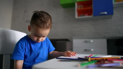 Un petit garçon caucasien est assis au bureau avec beaucoup de crayons de couleur.