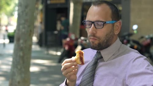 Young Businessman Eating Sandwich on Bench in City 30s