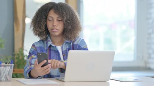 Young Woman Using Phone and Laptop Indoors