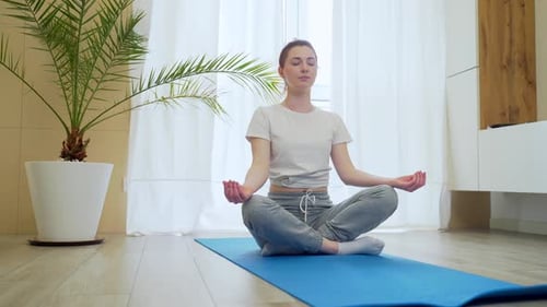 young redhead girl in lotus position practices yoga at home alone. Active woman in casual clothes