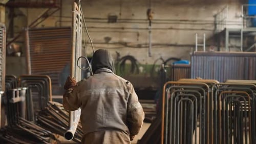 Arbeiter in Uniform trägt Metallrahmen aus Rohren in der Werkstatt