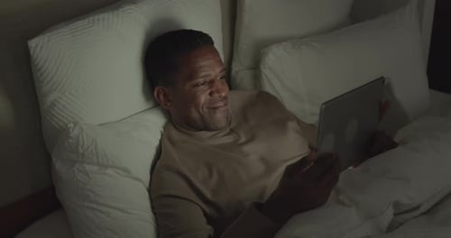 Man Relaxes in Bed Looking at Tablet
