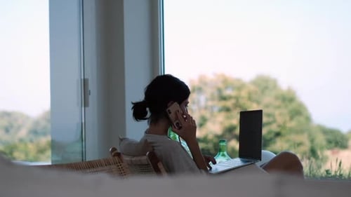 Woman on Laptop and Phone in Rural Home
