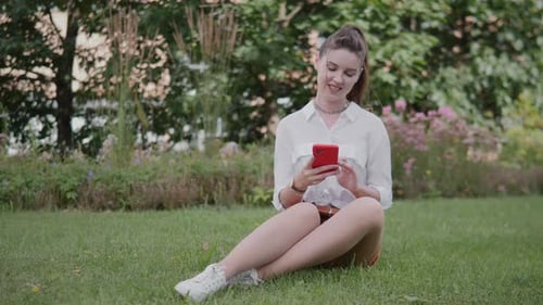 Businesswoman Enjoying a Break While Using Her Smartphone in a Garden During a Sunny Day