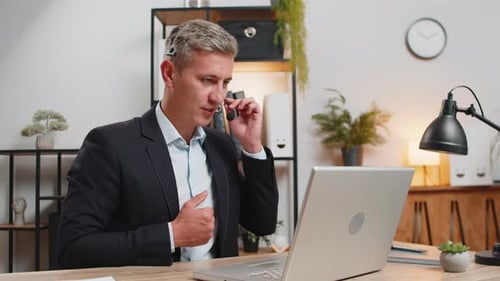 Confident Young Businessman in Headset Talking on Video Call Using Laptop Computer at Office Desk