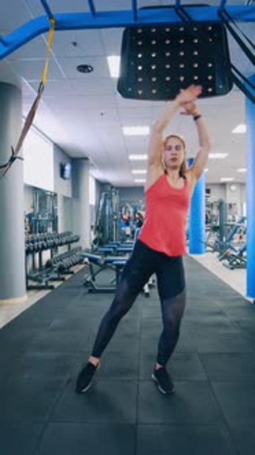 Full-length portrait of sportswoman in gym. Young girl doing exercise alone in a modern fitness club