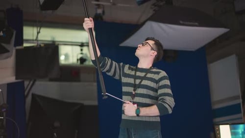 Man Holding Boom Microphone Adjusting in Studio Video Production Environment