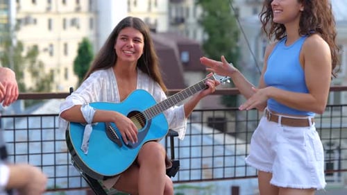 Young Woman Plays Guitar for Friends on Rooftop