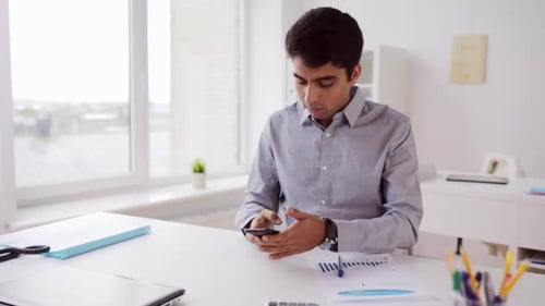 Young indian businessman browsing online statistics with smartphone in modern office