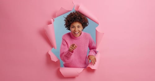 Glückliche Afroamerikanerin durchbricht Papier und zeigt lächelnd auf dich