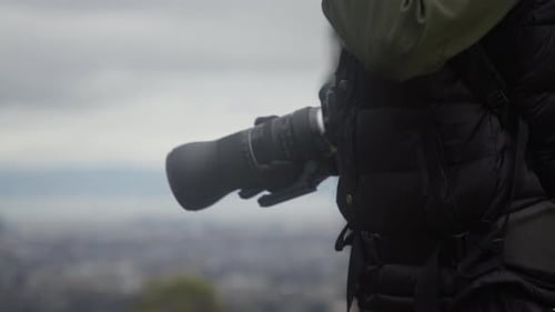 Photographer Holds Camera with Zoom Lens Overlooking City
